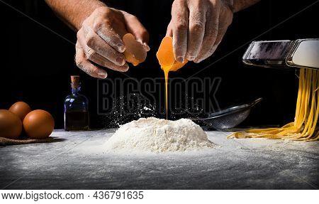 Man Making Pasta By Pouring Egg Into Flour Volcano And Background With Pasta Maker And Others