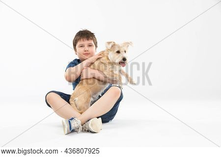 A Young Boy Sits On A White Background And In His Hands He Holds His Beloved Dog.