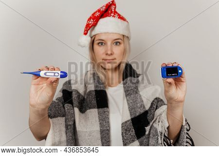 Woman In Santa Hat, Wrap And Protective Medical Mask Holds Thermometer And Puls Oximetr