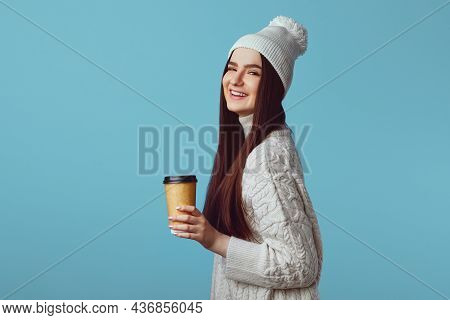 Happy Young Woman Wearing White Oversize Sweater And Hat Isolated Over Blue Background, Holding Take