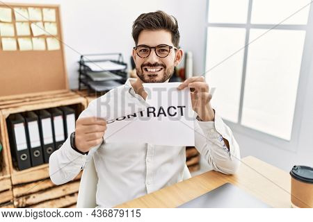 Young man with beard breaking contract paper at the office smiling with a happy and cool smile on face. showing teeth. 