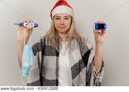 Woman In Santa Hat, Wrap And Protective Medical Mask Holds Thermometer And Puls Oximetr