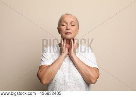 Mature Woman Doing Thyroid Self Examination On Beige Background