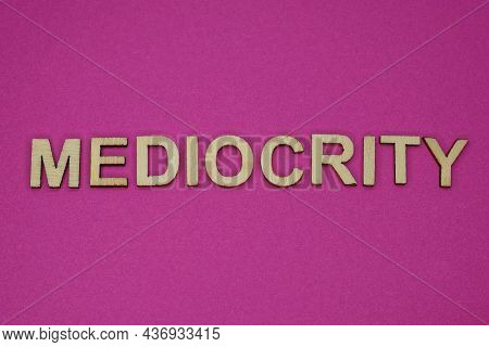 Word Mediocrity In Small Square Wooden Letters On A Pink Background