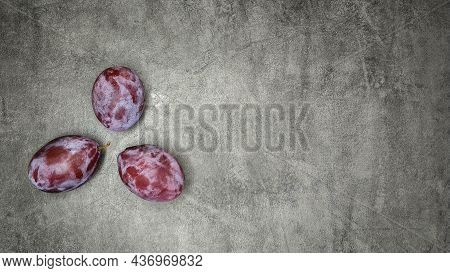 Three Fresh Plums On Gray Marble Background.