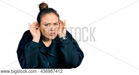 Young hispanic girl wearing sportswear trying to hear both hands on ear gesture, curious for gossip. hearing problem, deaf 