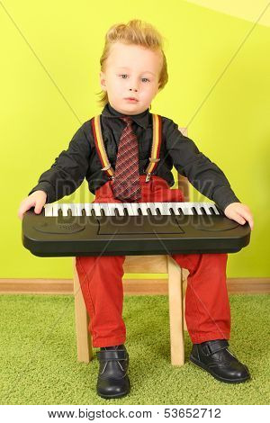 Little boy in bright clothes sitting on a chair with a toy piano on his knees