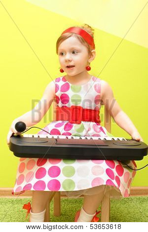 Mod little girl in a bright dress holding on her lap toy piano and microphone