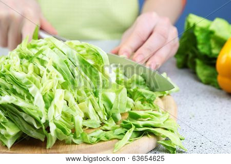 Female hands chopped cabbage on wooden board, close-up, on blue background