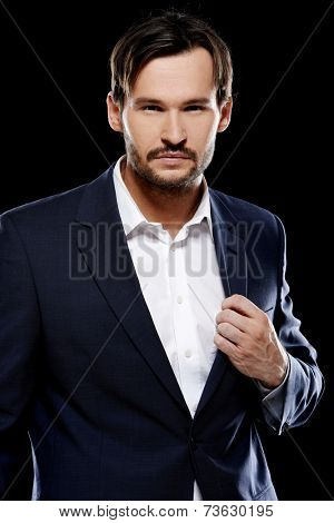 Handsome sexy stylish man in a smart jacket standing giving the camera a sultry seductive look  on a dark background
