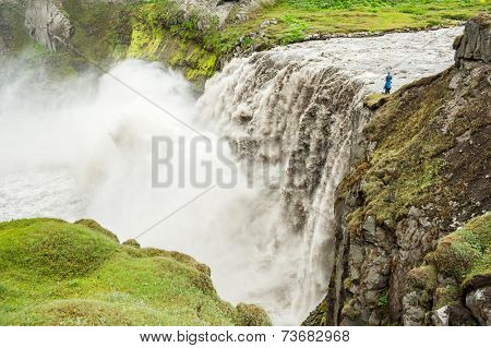 Unrecognizable photographer is taking pictures of Hafragilsfoss, very powerful waterfall. It is located in Jokulsargljufur National Park the northeasten Iceland on the river Jokulsa a Fjollum. 