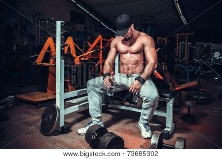 muscle shaped man tired sitting relaxed with weights and energy drink 