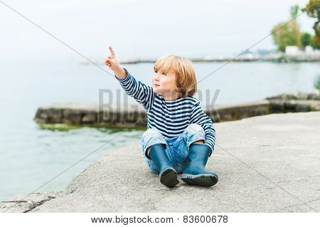Cute toodler boy having fun outdoors, playing by the lake on a rainy day