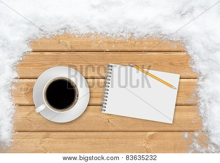 Coffee, pencil and notebook on the planks covered with snow