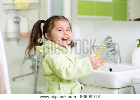Smiling little girl brushing teeth in bath