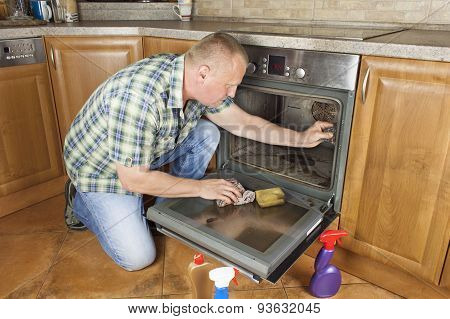 Man kneels on the floor in the kitchen and cleans the oven.
