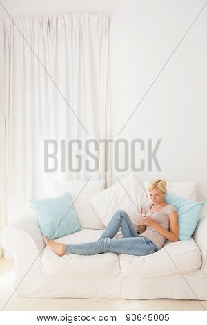 appy blonde woman using her mobile on the sofa at home in the living room