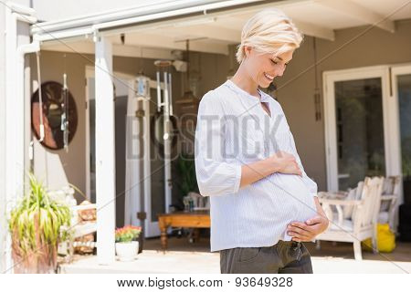 Smiling blonde pregnant handon hi belly at home