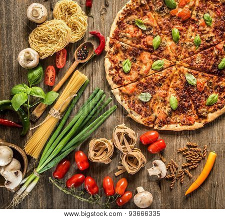 Italian food background with pizza, raw pasta and vegetables on wooden table