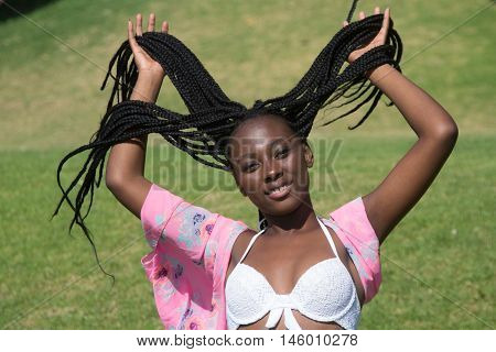 A gorgeous ethnic female in summer clothing holding her braids up with grass behind her