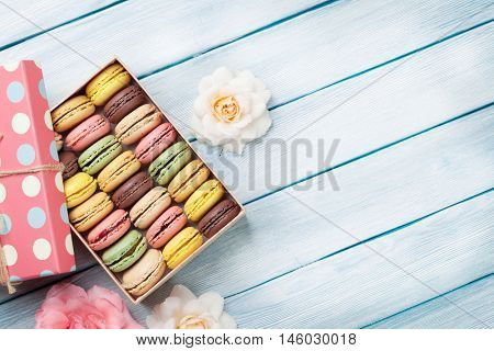 Colorful macaroons and rose flowers on wooden table. Sweet macarons in gift box. Top view with copy space for your text