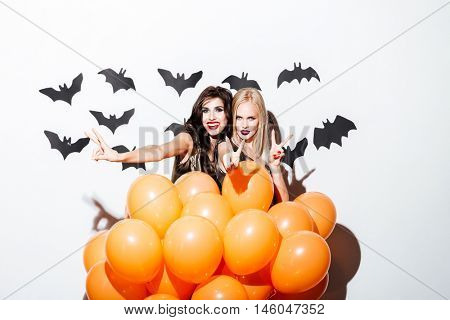 Two smiling beautiful women with vampire makeup and orange balloons having fun over white background