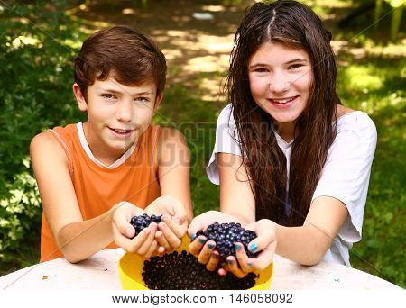 teenager siblings brother and sister with handful of bilberries close up smiling portrain on the green grass summer background