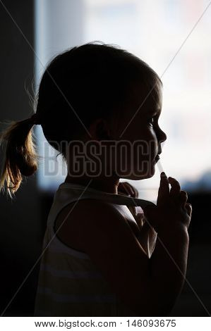 Silhouette of todler girl alone in the front of a window