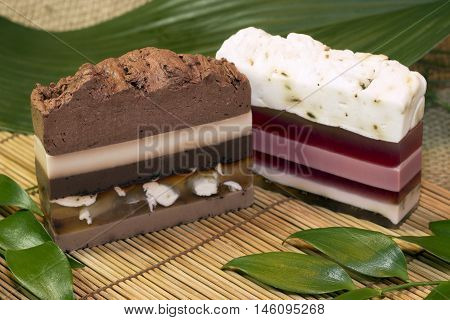 two bars of natural organic handmade soap in the form of piece of cake on a bamboo mat with green leaves