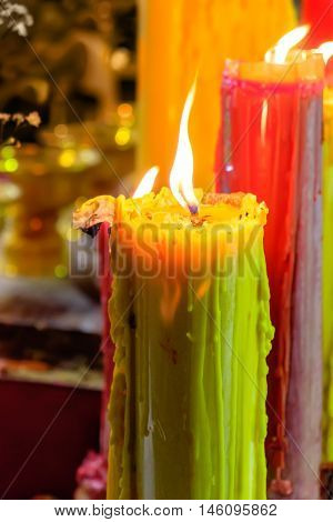 Burning red and yellow beautiful old textured candles with defocussed background of buddhist temple Thailand. Mood of sacrament and revelation.
