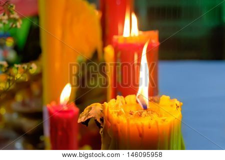 Burning red and yellow beautiful old textured candles with defocussed background of buddhist temple Thailand. Mood of sacrament and revelation.