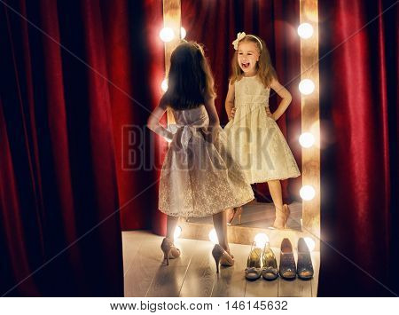 Cute little fashionista. Happy child girl try on outfits and mom's shoes looking at mirror.