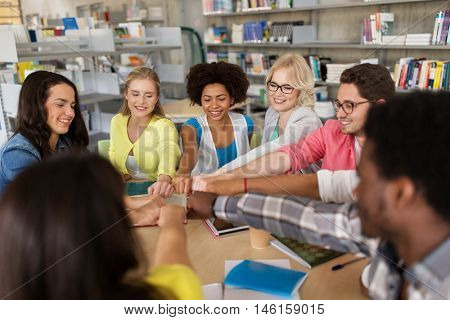 education, school, teamwork and people concept - group of international students sitting at table and making fist bump