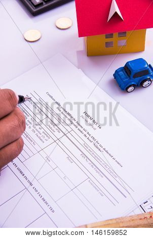 Indian man or accountant person filing Indian income tax returns form or ITR document showing indian currency, house model, toy car and calculator over white table top, selective focus