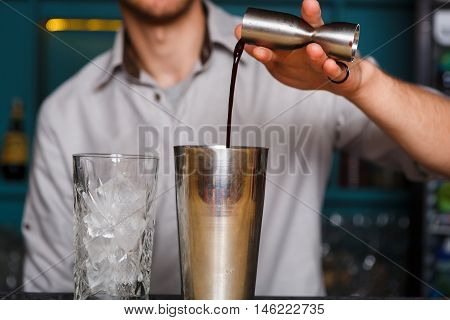 Barman's hands in bar interior making alcohol cocktail. Professional bartender at work in bar pouring drink into measuring glass. Party time in night club. Service industry occupation
