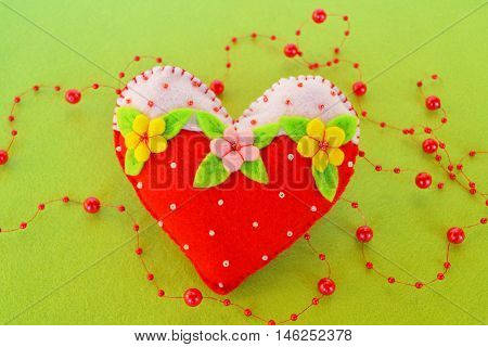 Hand stitched felt heart. Symbol of Valentines Day. Handmade felt toy on green background