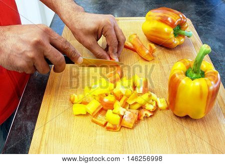 Man cutting stripy peppers on a wooden chopping board in the kitchen
