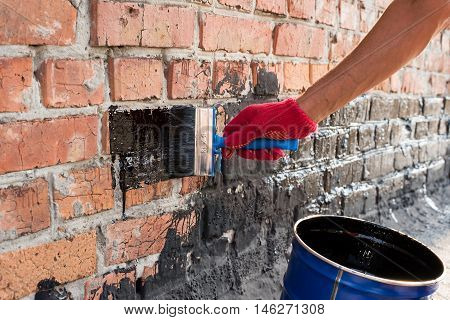 Roofer covered brick wall bitumen primer for improving adhesion during surfacing contiguity with rolled waterproofing during the installation of flat roof.
