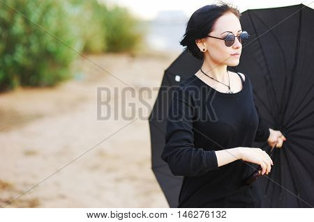 Beautiful Young Brunette Girl In Black Clothes With A Large Black Umbrella On The Shore Of The Bay T