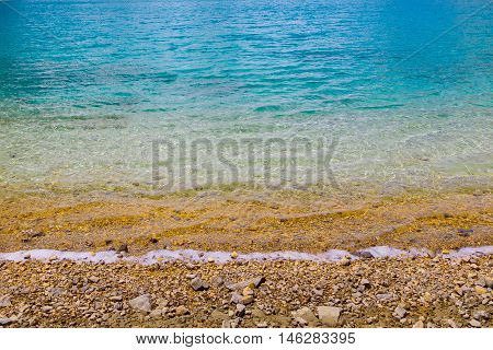 green blue water sea ocean background texture with brown pebbles.