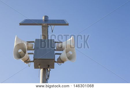 Solar-powered megaphones pole against blue sky background