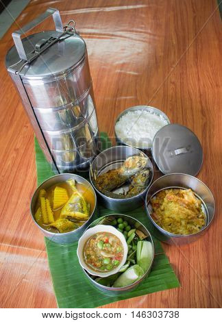thai food in food carrier thai styeomeletfried fishgreen curry chickenchili saurcevegetablerice
