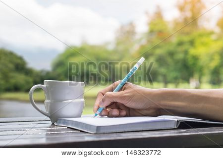 Work at park backgrounds concept. Coffee cup with book on wooden table under the spring sunlight in a park. Using as background or wallpaper