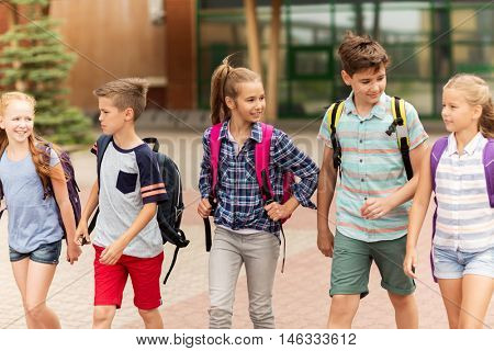 primary education, friendship, childhood, communication and people concept - group of happy elementary school students with backpacks walking and talking outdoors