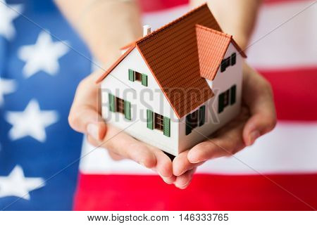 citizenship, residence, property, real estate and people concept - close up of hands holding living house model over american flag