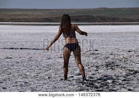 Woman walking along the dry bottom of a salt lake, rear view. Walk the dark-haired woman in a swimsuit on the bottom of a dry lake with salt and mud. The ancient dried-up lake.