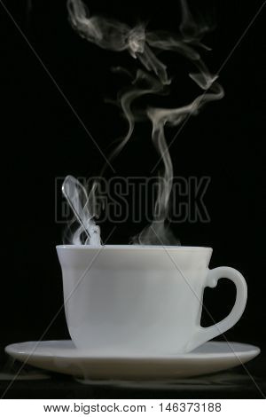 white cup with hot liquid and steam on black