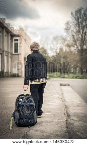 boy sadly goes to school with a heavy backpack