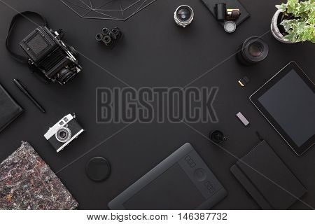 Work space on black table of a creative designer or photographer with laptop tablet cameras other objects of inspiration and copy space. Stylish home studio concept of technology trends.
