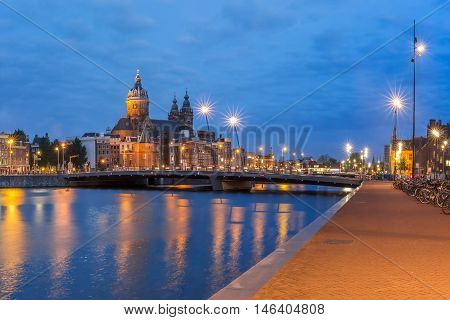 Night panoramic city view of Amsterdam canal, bridge and Basilica of Saint Nicholas, Holland, Netherlands. Long exposure.